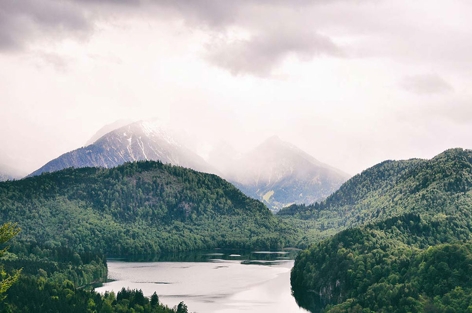 Blick auf einen See. Im Hintergrund kämpft sich der Berg durch die Nebeldecke